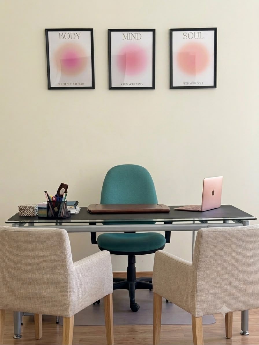 Scrivania dello studio con il computer e due poltrone per il colloquio, sotto tre quadri con le parole Body, Mind e Soul