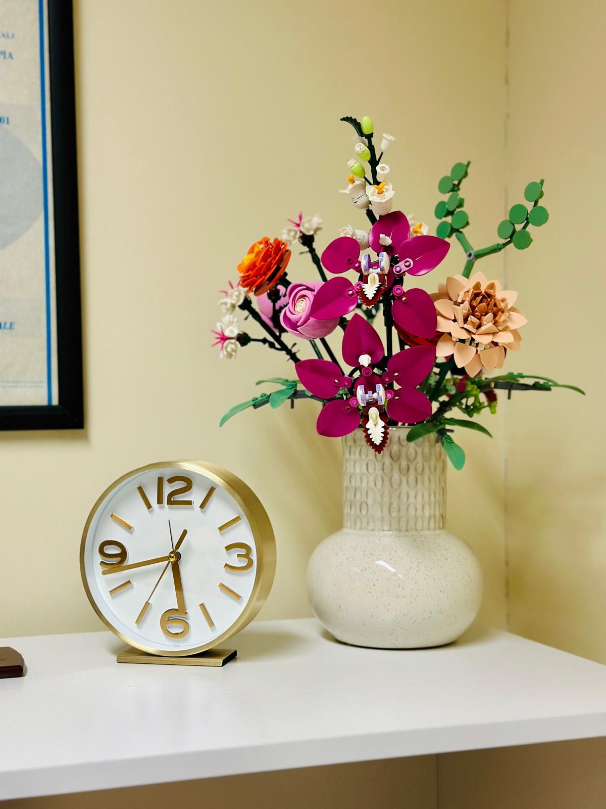 Dettaglio dello studio: un orologio da tavolo e un vaso di fiori su una mensola, accanto a un titolo professionale incorniciato